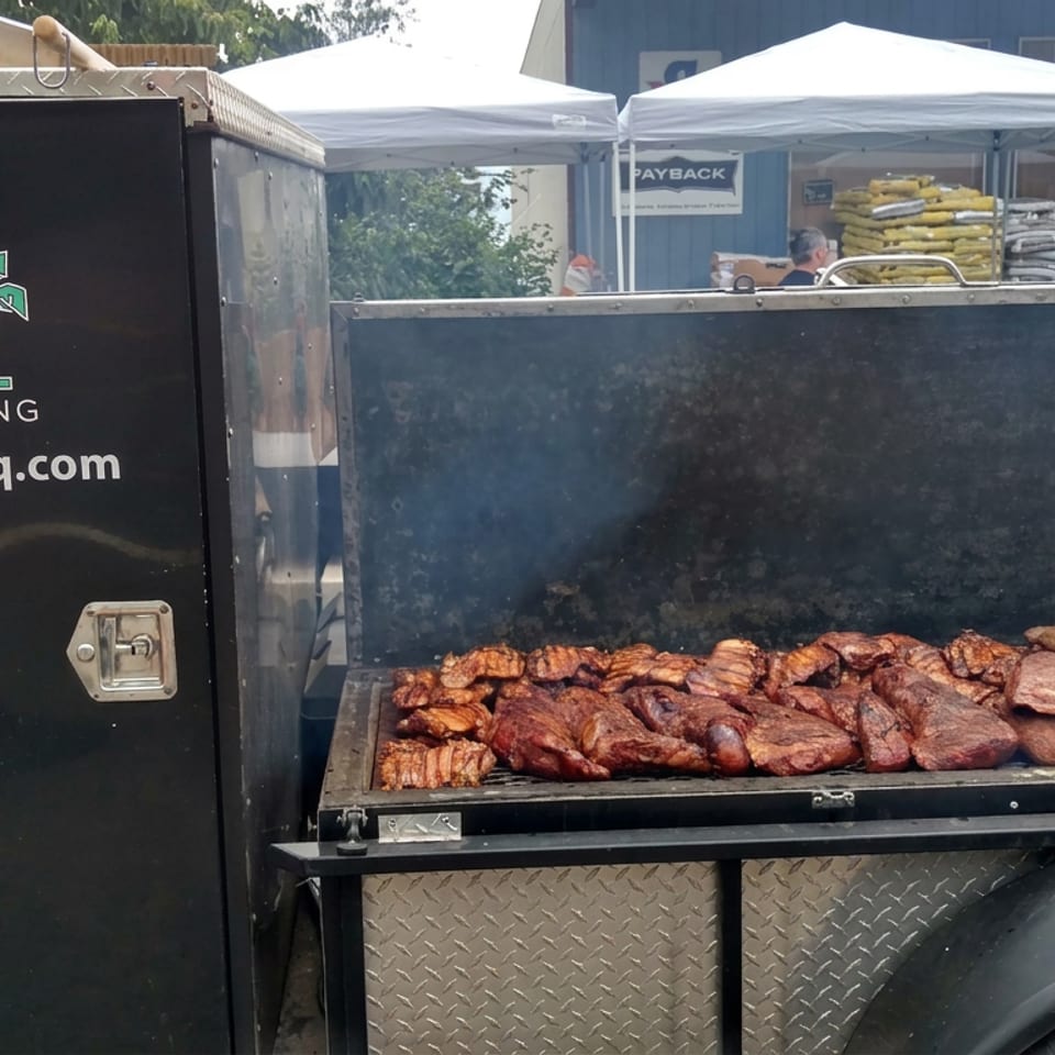 Big Kahuna’s Barbeque food truck grill loaded with smoked meats at an outdoor market.