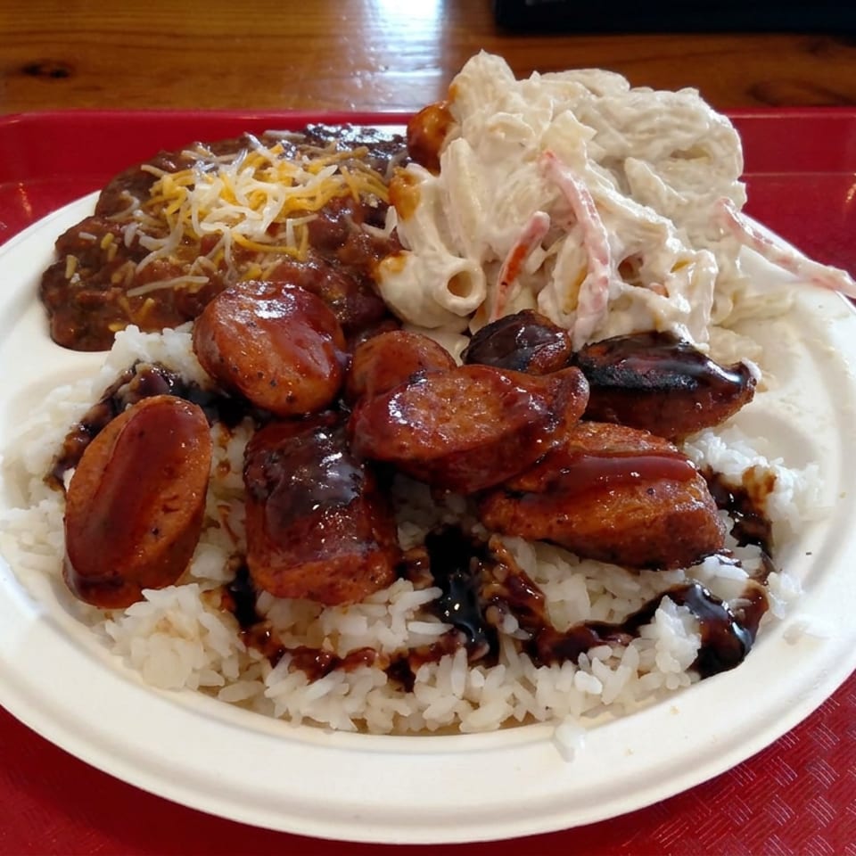 Plate of white rice topped with grilled sausage, black beans, shredded cheese, and creamy macaroni salad on a red tray.