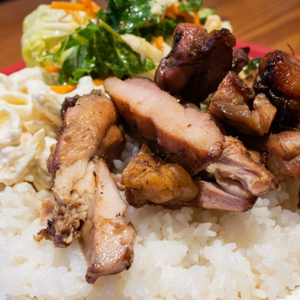 Plate of white rice topped with grilled meat, creamy pasta salad, and leafy green salad on a red tray.